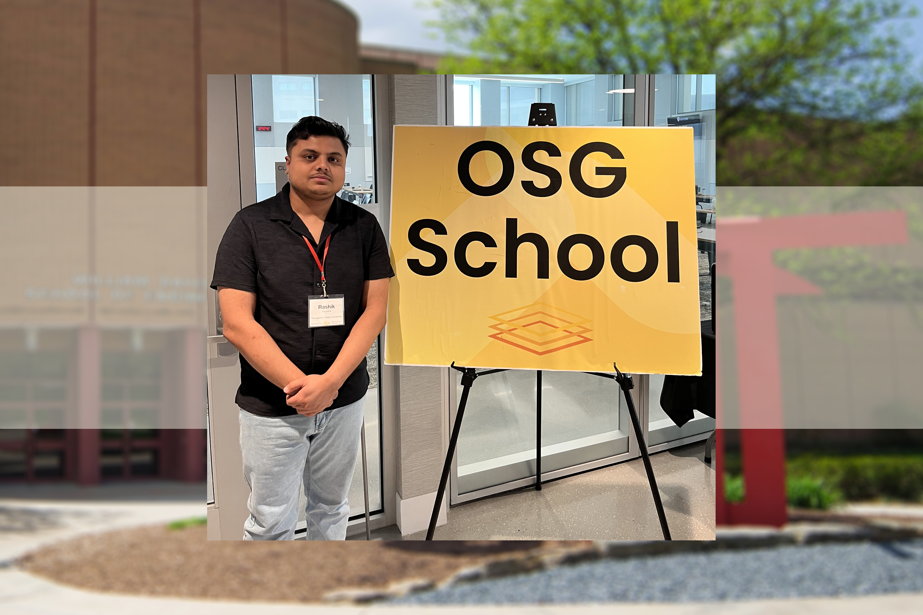 Rashik Neupane poses next to a sign that says OSG School