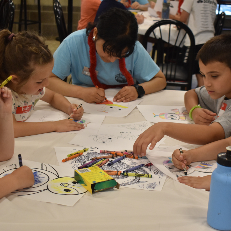 Camp counselor leading small group of children in coloring activity.