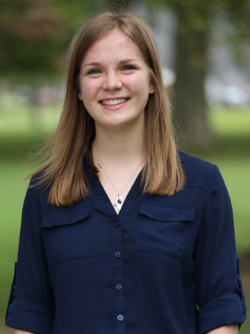 A smiling female student looking directly at the camera, wearing a navy blue blouse and posing outside