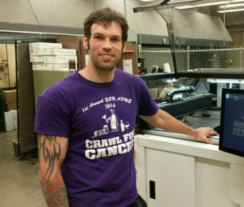 A male student with tattoos and a purple tshirt posing in a lab