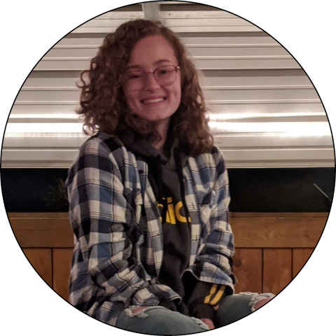 Rachael Thomas sits on the top of a table while smiling at the camera