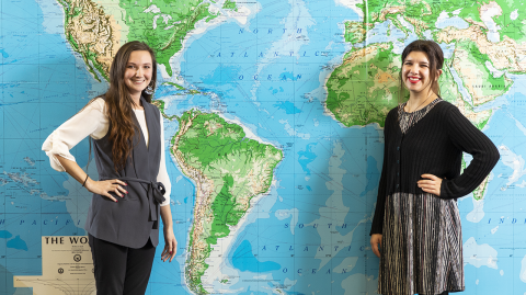Two female students posing in front of a large world map