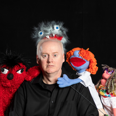 Professor Todd Dicken posing with four puppets
