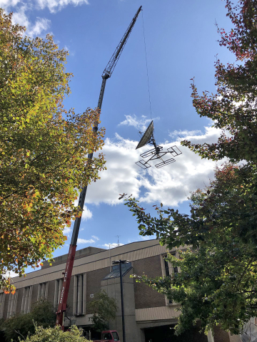  a giant crane removing old, outdated communications dishes and other equipment from the roof of Cus